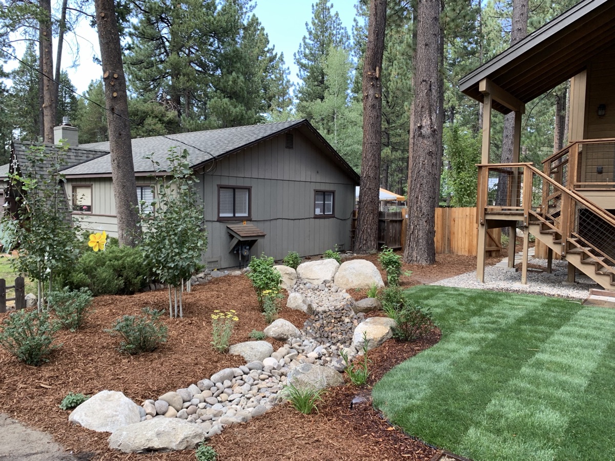 Dry creek drainage, river rock, mulch beds, boulders, and clean lawn edge at a Tahoe property